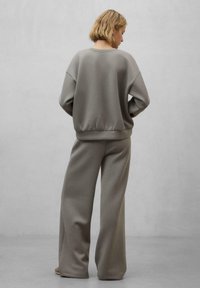 Felpa grigia e pantaloni larghi coordinati realizzati in tessuto morbido, con una vestibilità rilassata, polsini a coste e una trama liscia.