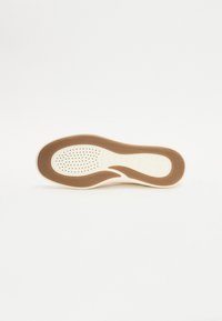 Helle Sneaker-Sohle mit einer strukturierten braunen Gummischicht und einer perforierten Innensohle für Atmungsaktivität. Ergonomisches Design für Komfort.