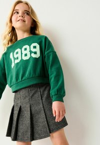 Grüner, kurzer Sweatshirt mit weißem "1989"-Grafik. Kombiniert mit einem grauen Hahnentrittmuster-gefalteten Rock. Weicher Stoff und lockere Passform.