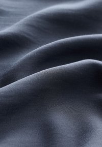 Tissu lisse gris foncé avec de légers plis et une texture mate douce visible en gros plan.