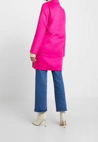 Cappotto in misto lana fucsia con maniche lunghe e taglio dritto, abbinato a jeans a gamba larga blu e stivaletti beige.