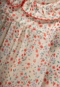 Tkanina s cvetnim vzorcem v kremni barvi, ki vsebuje male rdeče in vijolične rože ter zelene liste, z nabranim izrezom in nabranim dizajnom.