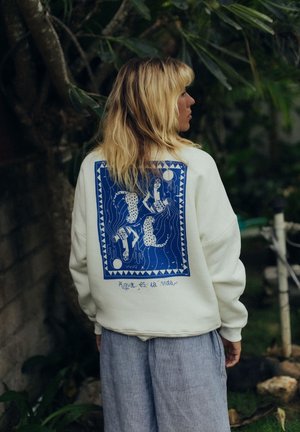 Biała bluza z niebieskim wzorem graficznym na plecach, przedstawiającym postacie w wodzie. Luźny krój, miękka faktura i casualowy styl.