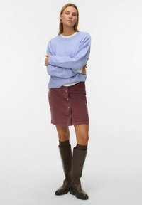 Licht paarse oversized trui, bordeauxrode corduroy rok met knopen aan de voorkant, bruine kniehoge laarzen en donkere sokken. Eenvoudige, casual outfit.