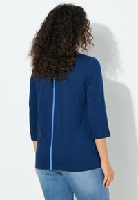 Laivastonsininen pusero, jossa on kolmivartiset hihat ja vaaleansininen pystyraita takana. Pehmeä kangas ja rento istuvuus.