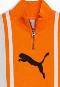 Suéter de punto naranja con un cuello alto, que presenta dos rayas blancas y un gran logo negro de Puma. Cierre de cremallera en el cuello.