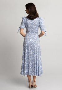 Jasnoniebieska sukienka do kolan z białym kwiatowym wzorem, z bufkami wiązanymi na kokardki i zwiewnym dołem. Uzupełniona o cieliste szpilki.