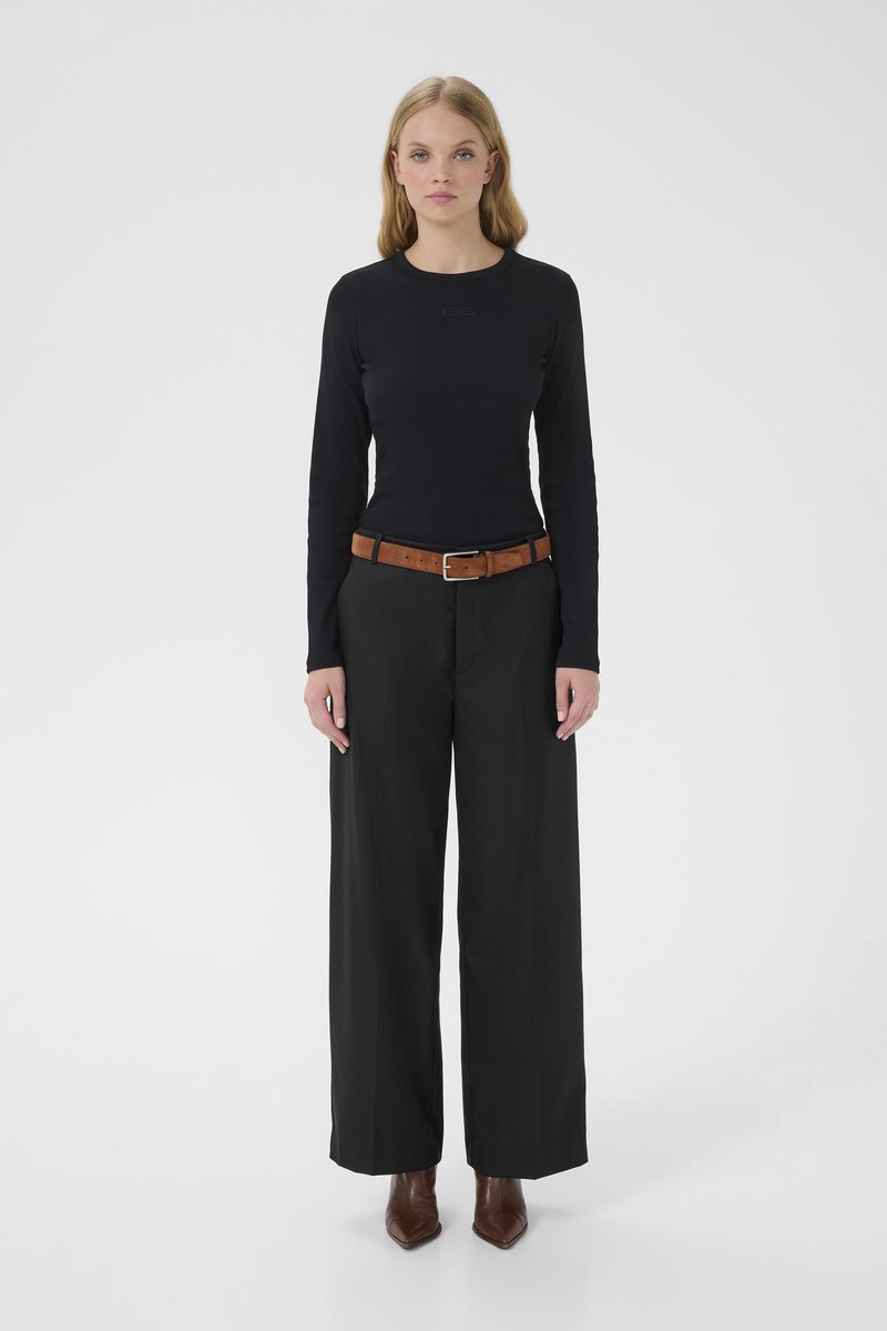 Haut noir à manches longues ajusté avec un col rond, associé à un pantalon noir taille haute à jambes larges et une ceinture en cuir marron. Bottines marron à bout pointu.