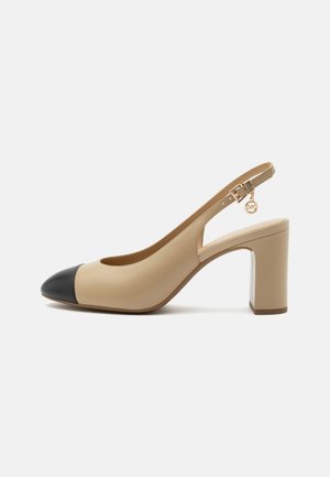 Chaussure à talon haut beige avec bride arrière, embout noir, bride réglable avec boucle et breloque dorée sur la bride.