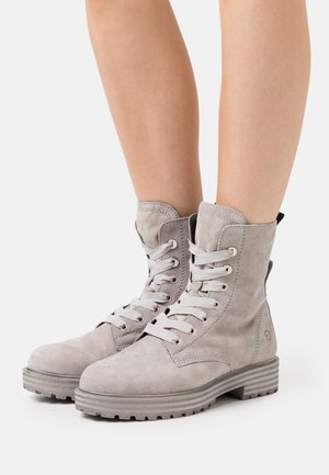 Botas de tobillo de ante gris con cordones, puntera redonda, suelas de goma y ojales plateados. Las botas cuentan con un talón reforzado y una lengüeta en la parte trasera.