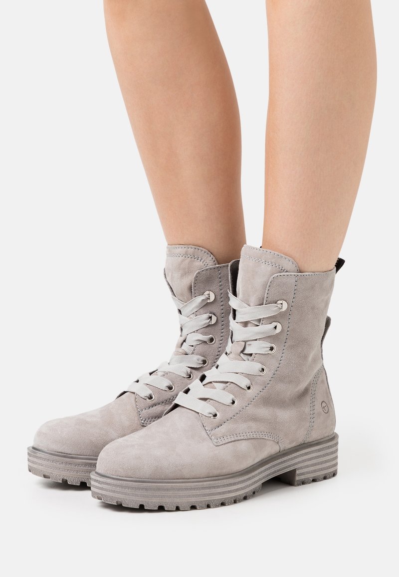 Bottines en suede gris à lacets, avec bouts ronds, semelles en caoutchouc et œillets en argent. Les bottines possèdent un talon renforcé et une languette.