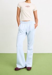 Beige aansluitend t-shirt met "Nike" logo, gecombineerd met lichtblauwe, relaxed-fit broek met een elastische tailleband en zijzakken, gedragen met kastanjebruine schoenen.