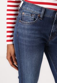 Dark blue denim jeans with a fitted design, featuring front pockets and subtle stitching details. The fabric has a smooth texture.