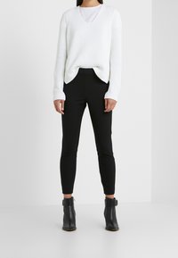 Biały prążkowany sweter z dekoltem w serek, połączony z czarnymi dopasowanymi spodniami i czarnymi botkami na kostkę. Strój cechuje się warstwowym wyglądem z kontrastem tekstur.