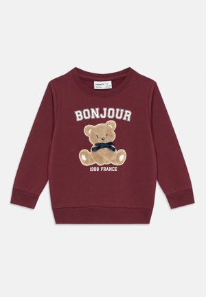 Sweatshirt de algodão cor marsala com decote redondo. Apresenta um urso bordado com um laço azul marinho e o texto "BONJOUR 1988 FRANCE" abaixo.