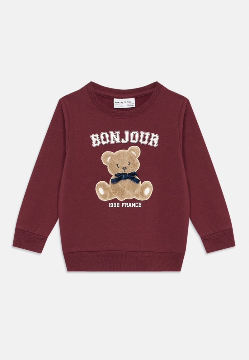 Maroon pamučna dukserica s okruglim izrezom. Na njoj se nalazi vezeni medo s mornarsko plavim mašnom i tekst "BONJOUR 1988 FRANCE" ispod.