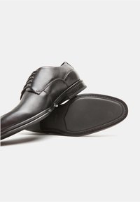 Scarpe eleganti in pelle nera con finitura liscia, punta arrotondata, design con lacci e suola in gomma testurizzata per una maggiore aderenza.