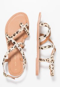 Sandály s leopardím vzorem a překříženými pásky, béžovou plochou podrážkou a zlatými kovovými doplňky. Měkký materiál s texturovaným povrchem.