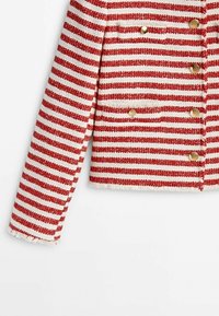 Veste rayée rouge et blanche en tissu texturé, avec un design court, des boutons dorés et des bords effilochés sur les manches.