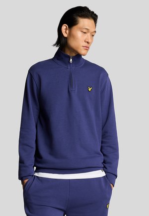Navy blue zip-up sweatshirt with a high collar, soft texture, and a small yellow logo on the chest. Matching pants complete the outfit.