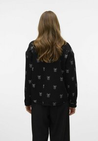 Zwarte langemouwen shirt met een herhaald wit strikpatroon. Zachte, textuurstof met een relaxte pasvorm en knoopmanchetten.