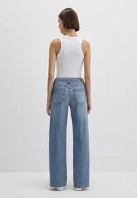 White ribbed tank top paired with light blue wide-leg jeans, featuring a back patch and two back pockets. Smooth fabric texture.