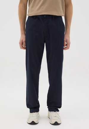 Marineblauwe katoenen broek met een rechte pasvorm, sluiting met knoop aan de voorkant en zijzakken. Gekocht met lichtgekleurde sneakers.