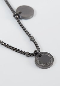 Metallkette mit schwarzem Band und zwei runden Anhängern. Ein Anhänger trägt die eingravierte Aufschrift "LIEBESKIND." Strukturierte Oberfläche mit polierten Akzenten.