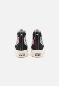 Schwarze Leinenschuhe mit hohem Schaft und floralem Stickmuster. Weiße Gummisohle und Zehenkappe, mit "CONVERSE ALL★STAR"-Markierung an der Ferse.