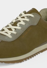 Baskets en daim marron et gris avec des lacets blancs et une semelle texturée, marquées "Michael Kors" sur la tige latérale.