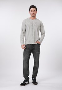 Μπλούζα με μακριά μανίκια σε γκρι και λευκές ρίγες, σε συνδυασμό με μαύρο τζιν ίσιας γραμμής. Το μοντέλο φοράει μαύρα αθλητικά παπούτσια με λευκές ρίγες. Απλό, καθημερινό στυλ.