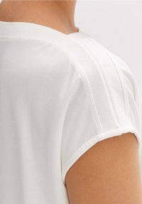 T-shirt bianco in cotone con maniche corte arrotolate e scollatura leggermente a giro. Tessuto liscio con cuciture minime.