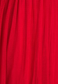 Tissu plissé rouge avec une surface texturée, présentant de subtiles rayures verticales et de petits points en relief. Drapé fluide et couleur vive.