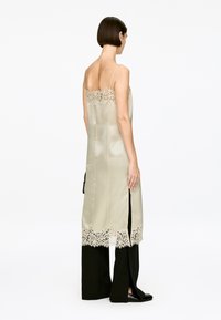 Langes Seidenkleid in hellem Creme mit aufwendiger Spitzenverzierung am Ausschnitt und dem Saum; verfügt über seitliche Schlitze und verstellbare Spaghettiträger.