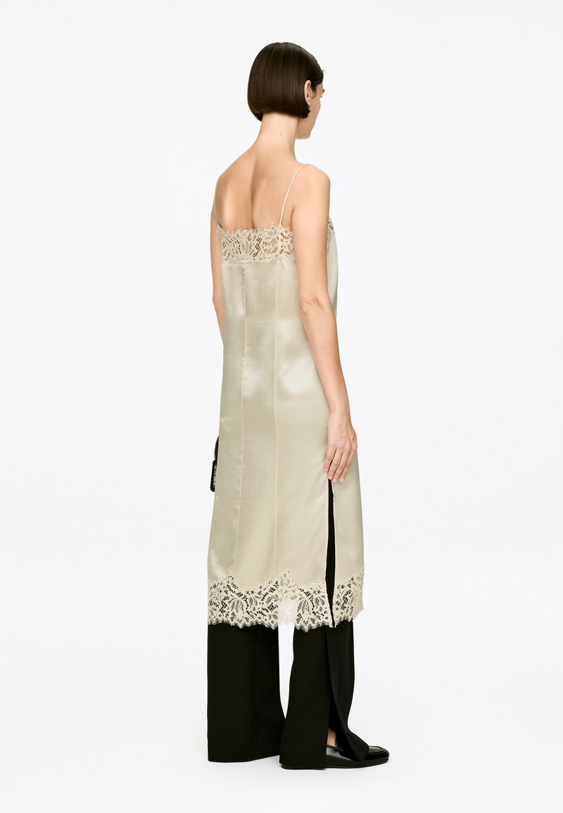 Langes Seidenkleid in hellem Creme mit aufwendiger Spitzenverzierung am Ausschnitt und dem Saum; verfügt über seitliche Schlitze und verstellbare Spaghettiträger.