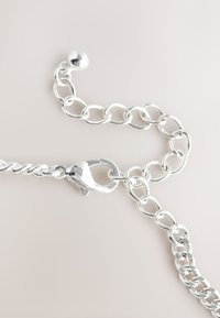 Silver metal chain featuring oval links with a twisted section. Includes a round bead and a secure lobster clasp. Smooth, shiny surface.