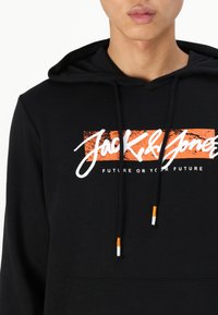 Sudadera negra con un bolsillo frontal, que presenta el texto blanco y naranja 'Jack & Jones' y 'FUTURE OR YOUR FUTURE' en el pecho. Cuerdas ajustables.