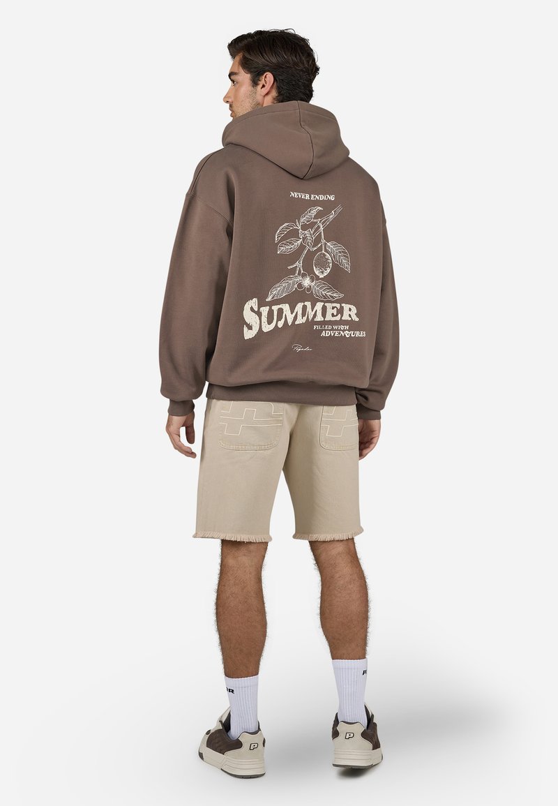 Brun hoodie med grafisk tryk af blade og ordet "SOMMER" på ryggen, parret med beige slidte shorts og sneakers.