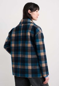 Karirana volnena plašča v mornarski, bež in teal barvi. Ima ovratnik in širok kroj. Mehka tekstura s karirastim vzorcem po celotni površini.