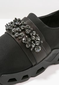 Chaussure noire à enfiler avec une semelle en caoutchouc épaisse et un cluster décoratif de petits cristaux ronds clairs sur la bride supérieure.