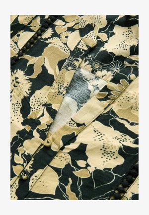 Floral patterned fabric in beige and black features a placket with gold buttons and decorative pom-pom trim along the edges.