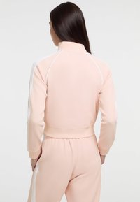 Perzikkleurige, aansluitende trainingsjack met een hoge kraag, witte zijstrepen en ribgebreide manchetten. Zacht, glad materiaal met een cropped ontwerp.