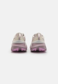 Baskets de sport rose clair avec une tige en maille, semelles rembourrées et accents violets sur le talon et la semelle extérieure. Présente une finition douce et texturée.