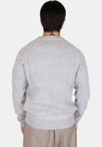 Maglione grigio a coste con maniche lunghe, spalle raglan e vita aderente, che mostra una texture morbida e un design minimalista.