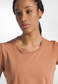 Lyhythihainen paita haalistuneessa terrakotan värissä, jossa on pyöreä pääntie ja pehmeä, teksturoitu kangas. Yksinkertainen muotoilu ilman kuvioita tai koristeita.