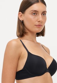 Black padded bra with adjustable straps, smooth texture, and a seamless design. Features a simple, minimalistic style and soft fabric.