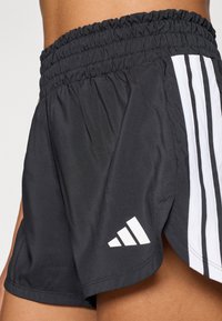 Fekete sportnadrág elasztikus derékpánttal, fehér háromcsíkos díszítéssel és fehér logóval az alsó szegélyen. Puha, könnyű anyagból.