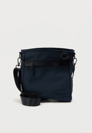 Marineblaue Umhängetasche mit verstellbarem Schultergurt, vorderer Reißverschlusstasche und Metallring-Detail auf glatter Stoffoberfläche.