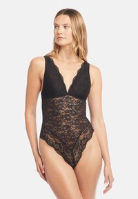 Černý krajkový body s hlubokým výstřihem do V, květinovým vzorem, zvlněnými okraji a průsvitným designem. Nastavitelné ramínka pro přizpůsobení velikosti.