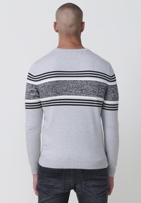Suéter gris de punto con un patrón texturizado de rayas en blanco y negro en el pecho, cuello redondo y mangas largas. Diseño ajustado.